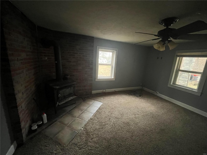 Unfurnished living room featuring carpet, ceiling fan, and a wood stove