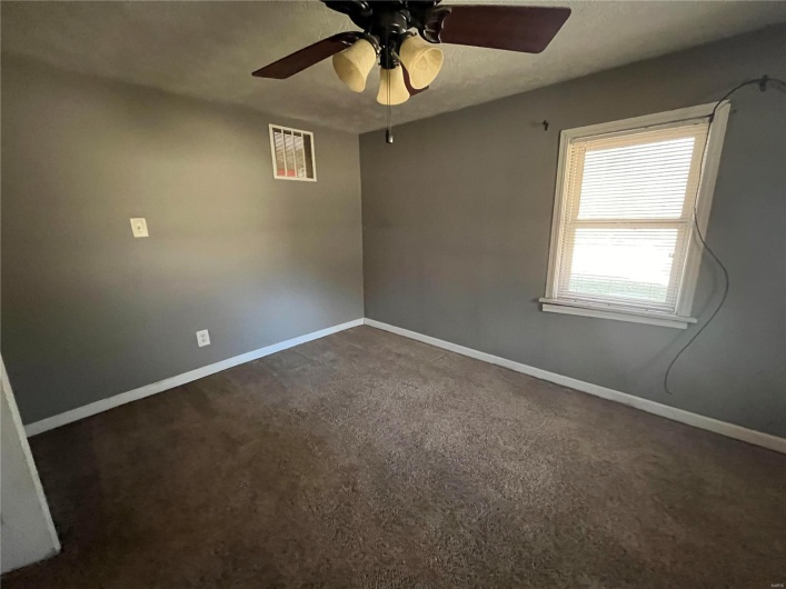 Empty room with ceiling fan and dark carpet