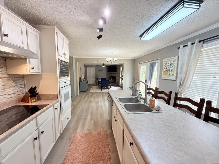 Kitchen with a textured ceiling, white cabinetry, a sink, a glass covered fireplace, and white oven