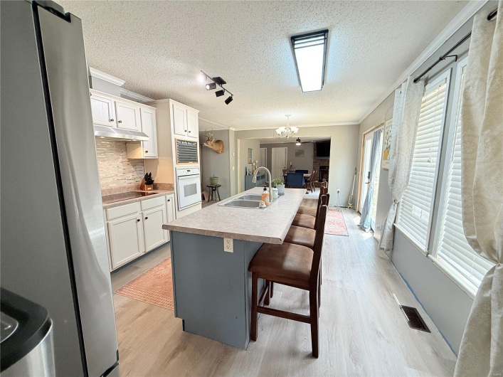 Kitchen featuring freestanding refrigerator, under cabinet range hood, oven, a sink, and a notable chandelier