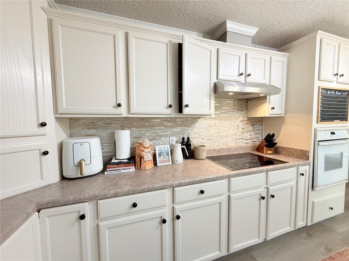Kitchen featuring under cabinet range hood, black electric cooktop, tasteful backsplash, crown molding, and oven