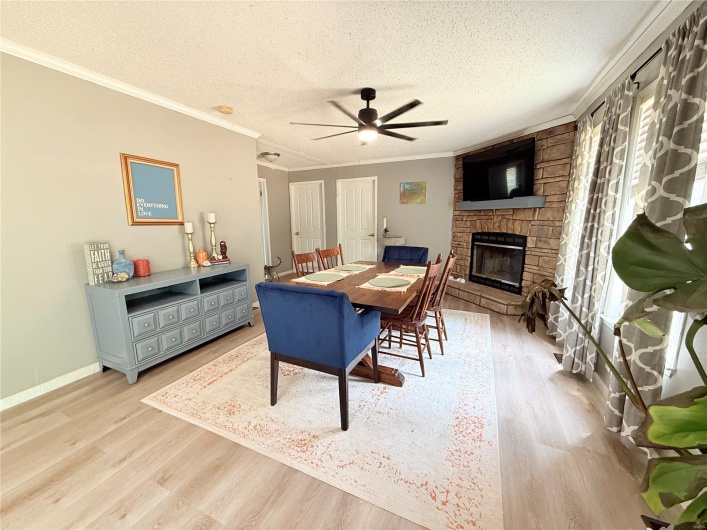 Dining room featuring a ceiling fan, a textured ceiling, a stone fireplace, and light wood finished floors