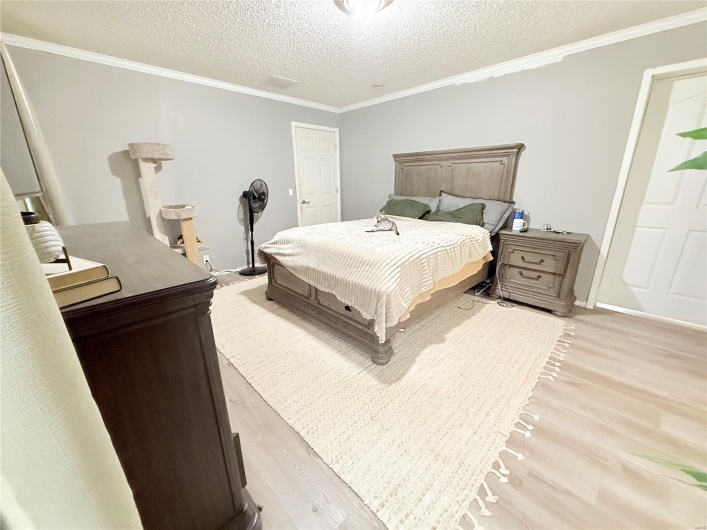 Bedroom with baseboards, light wood-style floors, a textured ceiling, and crown molding