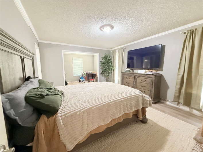Bedroom featuring a textured ceiling, light wood-style floors, and ornamental molding