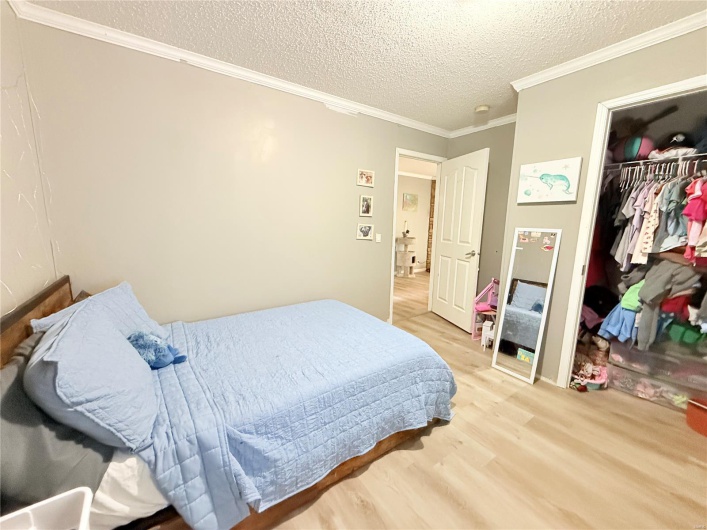 Bedroom featuring a closet, crown molding, a textured ceiling, and light wood finished floors
