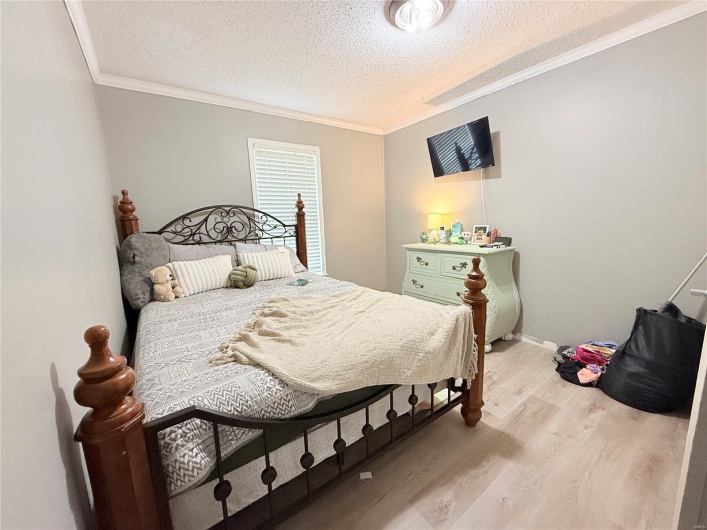 Bedroom featuring baseboards, wood finished floors, a textured ceiling, and ornamental molding