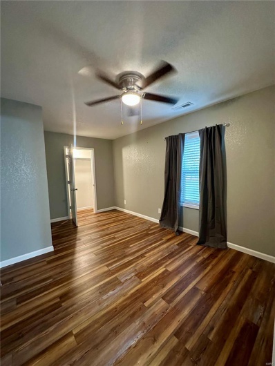 Spare room with a ceiling fan, visible vents, baseboards, and dark wood-type flooring
