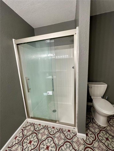 Full bathroom featuring a textured ceiling, a stall shower, baseboards, toilet, and tile patterned flooring