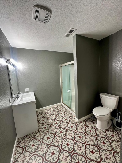 Bathroom with baseboards, visible vents, a shower stall, and toilet