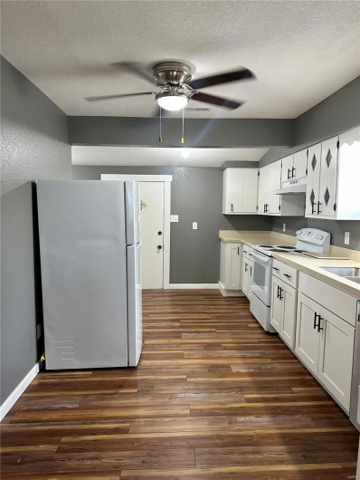 Kitchen with baseboards, white appliances, under cabinet range hood, and dark wood-style floors