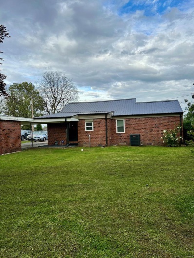 Back of house featuring brick siding, metal roof, a carport, cooling unit, and a lawn