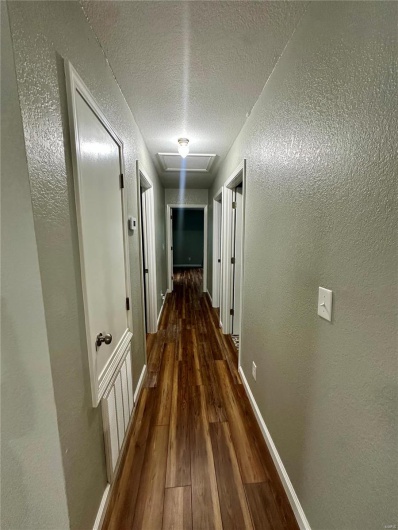 Hallway with a textured ceiling, a textured wall, dark wood-style floors, and baseboards