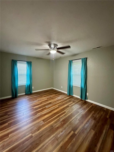 Spare room with wood finished floors, ceiling fan, plenty of natural light, and visible vents