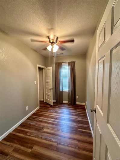 Unfurnished room with baseboards, ceiling fan, a textured ceiling, and dark wood-style flooring