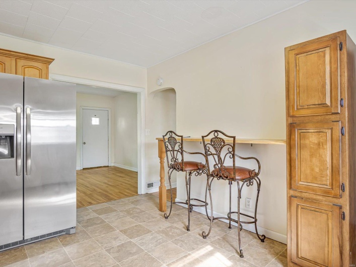 Kitchen featuring arched walkways, brown cabinets, baseboards, and stainless steel fridge with ice dispenser