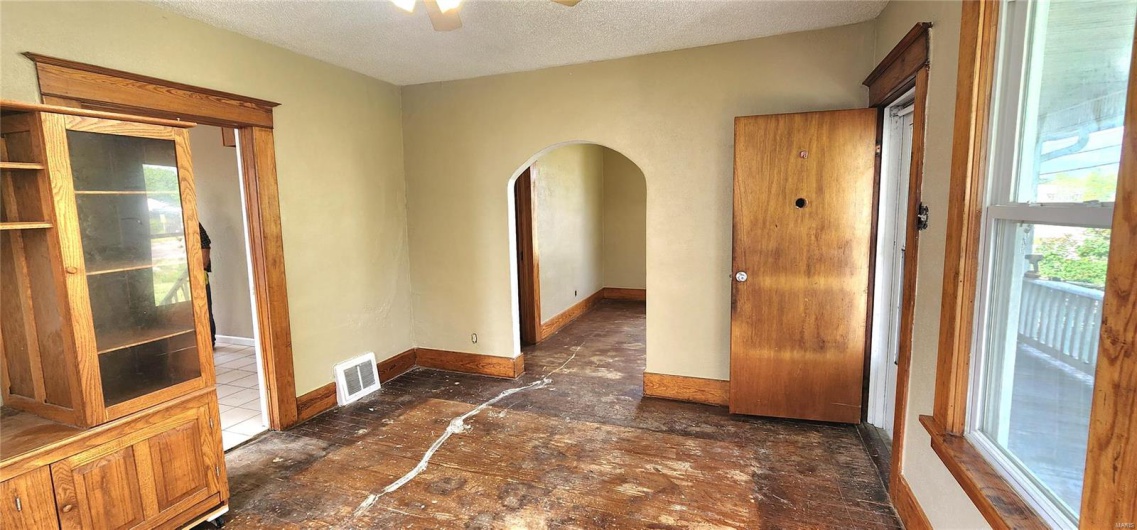 Spare room featuring a textured ceiling, ceiling fan, visible vents, baseboards, and arched walkways