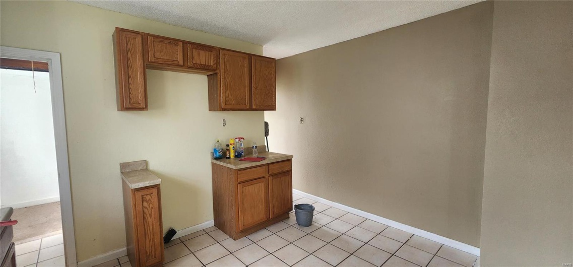Kitchen featuring light tile patterned floors, light countertops, brown cabinetry, and a textured ceiling