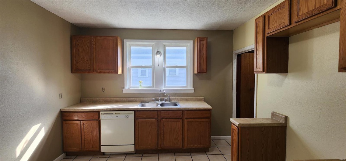 Kitchen with a textured ceiling, brown cabinets, dishwasher, and a sink