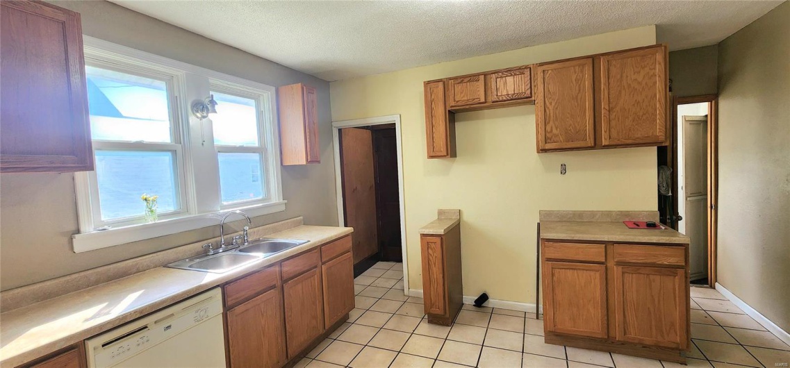 Kitchen featuring light tile patterned floors, a textured ceiling, brown cabinets, a sink, and dishwasher