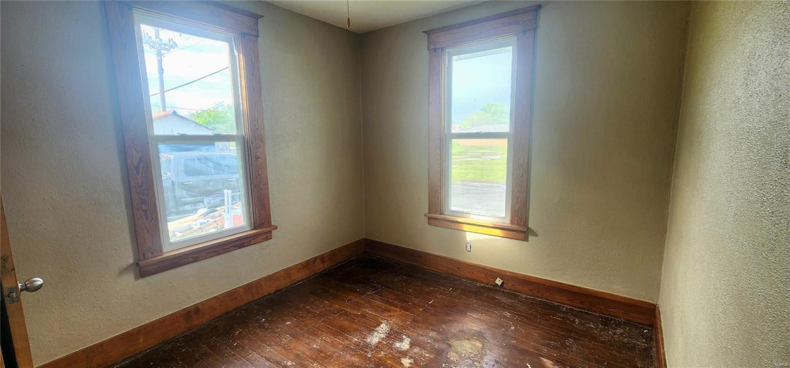 Main floor bedroom room featuring dark wood-type flooring, a textured wall, and baseboards