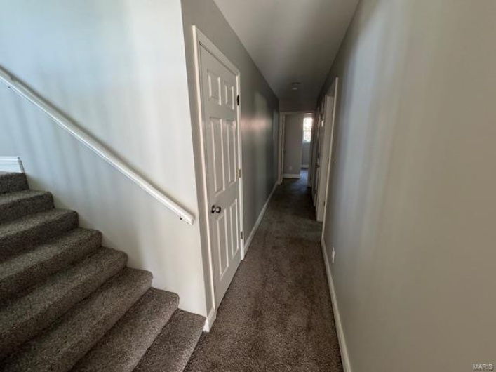 Hall featuring baseboards, dark carpet, and stairway