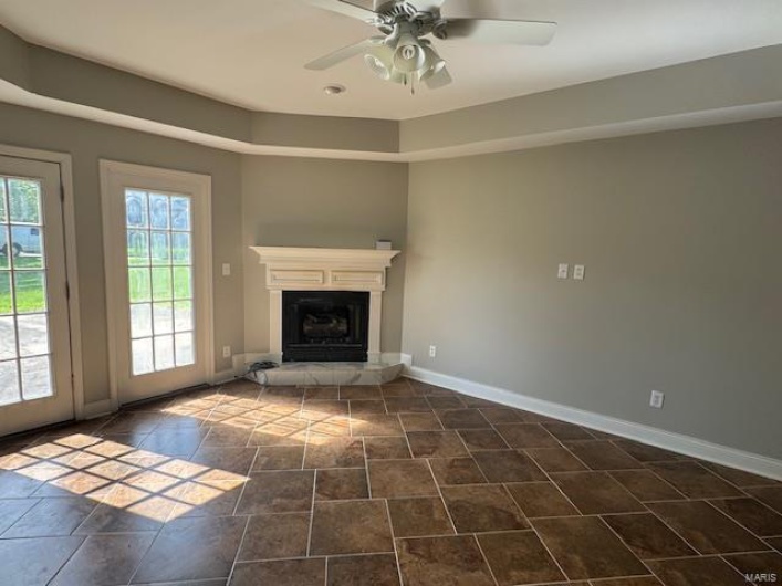 Unfurnished living room featuring a glass covered fireplace, baseboards, and ceiling fan