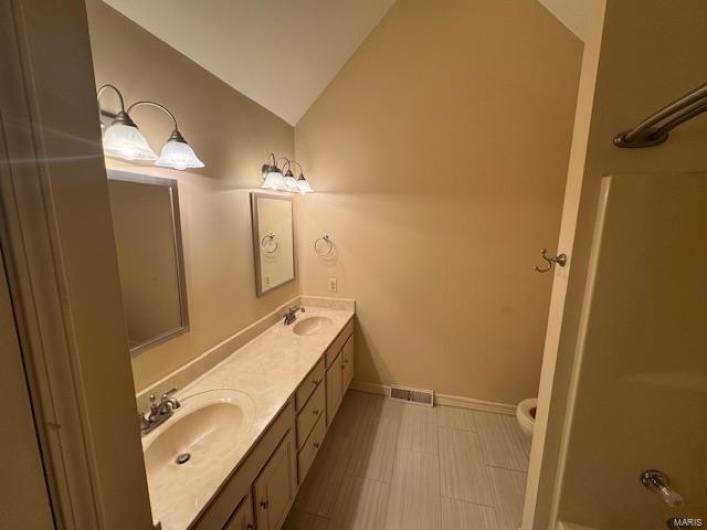 Full bath featuring double vanity, vaulted ceiling, a sink, and visible vents