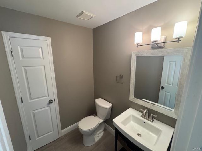 Bathroom featuring vanity, baseboards, wood finished floors, and toilet