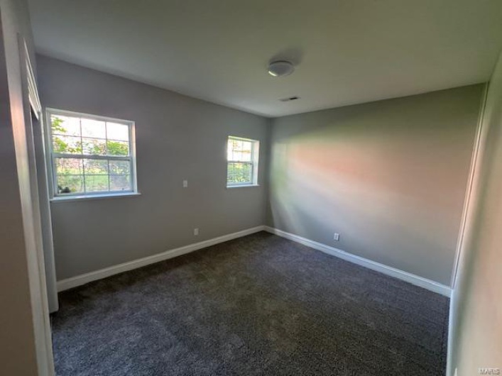 Unfurnished room featuring baseboards and dark carpet