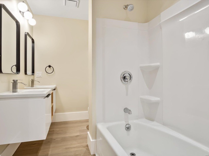 Full bath featuring a sink, shower / bath combination, double vanity, baseboards, and wood finished floors