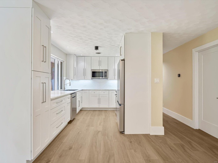 Kitchen with white cabinetry, stainless steel appliances, light wood-type flooring, and a sink