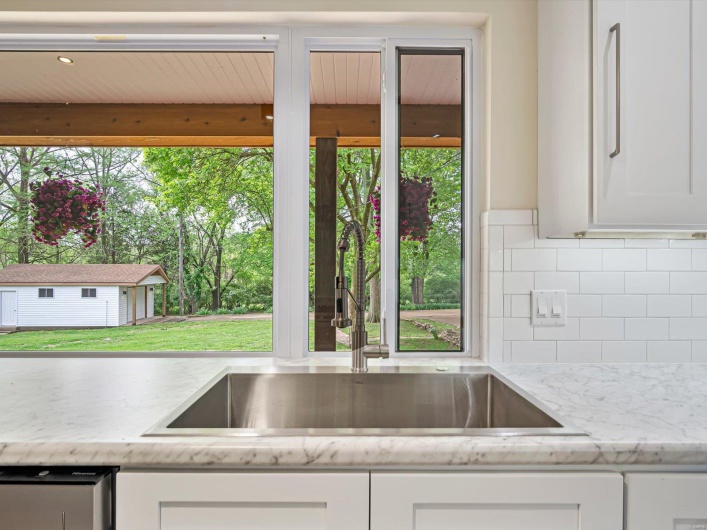 Kitchen with white cabinets, backsplash, light stone counters, and a sink