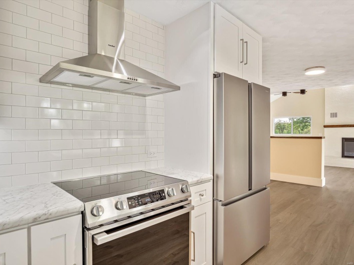 Kitchen featuring stainless steel appliances, decorative backsplash, white cabinetry, wall chimney range hood, and baseboards