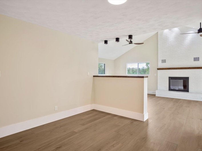 Unfurnished living room featuring baseboards, wood finished floors, a ceiling fan, and a textured ceiling
