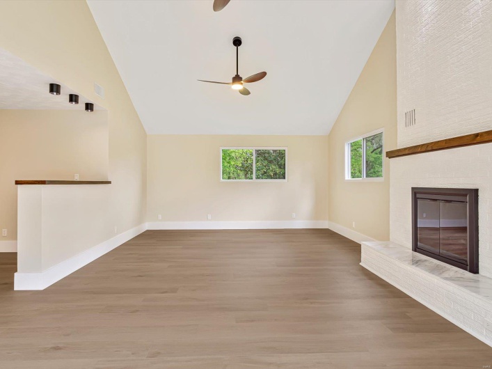 Unfurnished living room with a fireplace, ceiling fan, high vaulted ceiling, baseboards, and wood finished floors