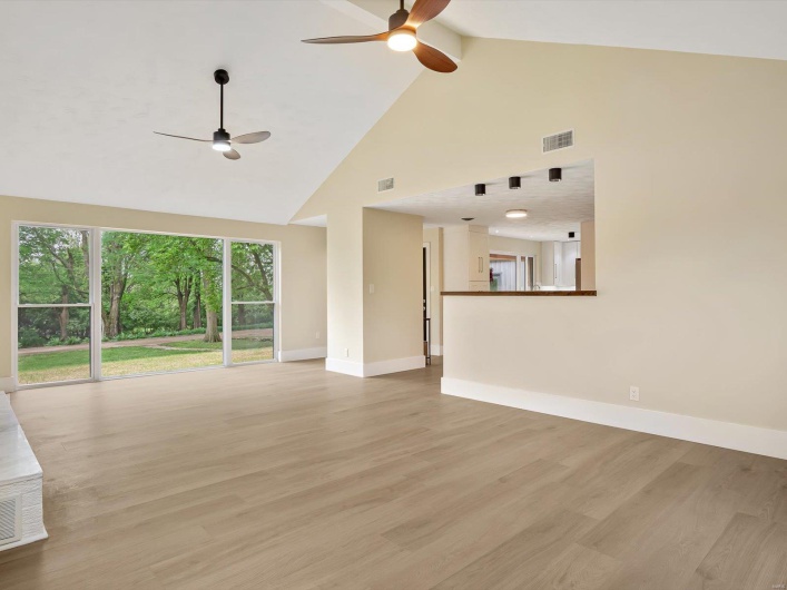 Unfurnished living room with light wood-style floors, visible vents, baseboards, a ceiling fan, and high vaulted ceiling