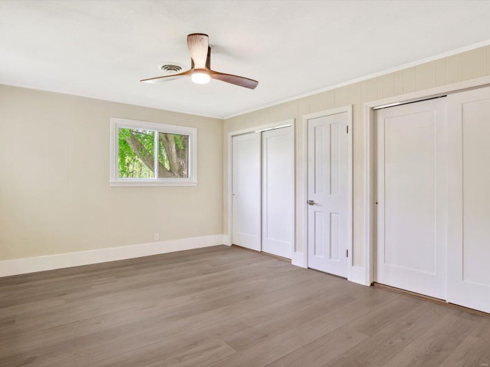 Unfurnished bedroom featuring baseboards, light wood-type flooring, crown molding, and multiple closets