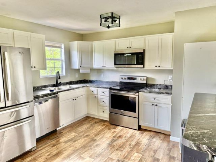Kitchen with white cabinets, stainless steel appliances, dark countertops, and a sink
