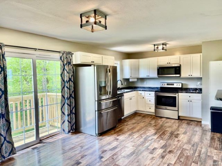 Kitchen with stainless steel appliances, dark countertops, dark wood finished floors, and a sink