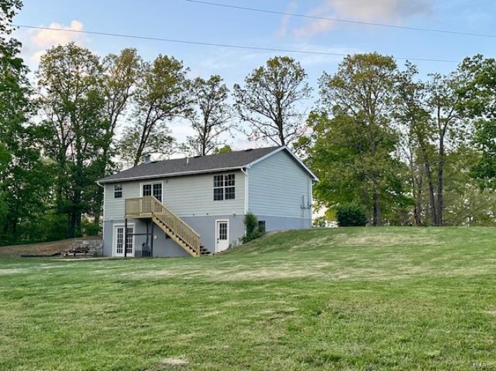 Back of property featuring a yard, a wooden deck, and stairs