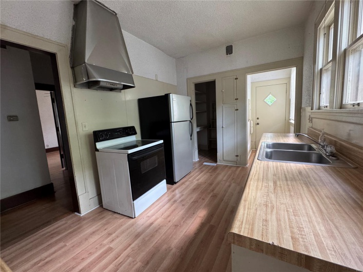 Kitchen with light wood-type flooring, a sink, range with electric cooktop, and wall chimney range hood