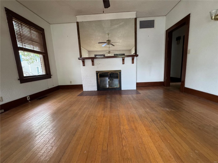 Unfurnished living room featuring a ceiling fan, visible vents, a fireplace with flush hearth, and hardwood / wood-style flooring