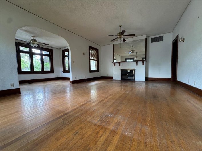 Unfurnished living room featuring wood-type flooring, ceiling fan, visible vents, and plenty of natural light