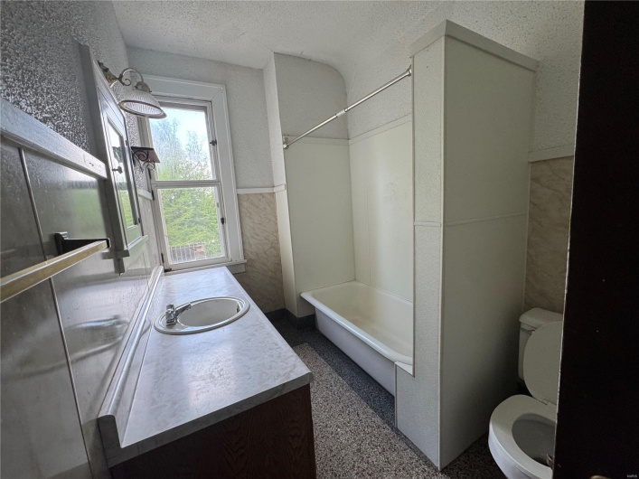 Full bath with vanity, wainscoting, toilet, bathtub / shower combination, and a textured ceiling