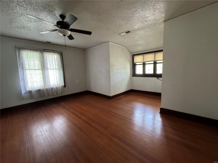 Empty room featuring visible vents, a ceiling fan, a textured ceiling, and dark wood-type flooring