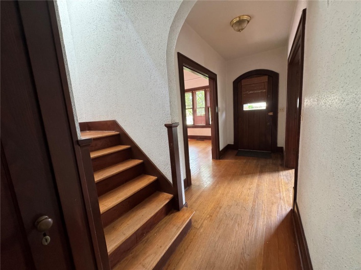 Entryway featuring arched walkways, a textured wall, stairs, and wood finished floors