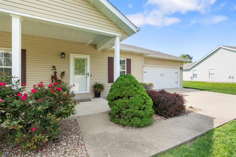 Doorway to property featuring a garage, a porch, a shingled roof, and driveway