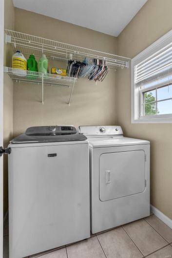 Clothes washing area with laundry area, washer and clothes dryer, baseboards, and light tile patterned floors