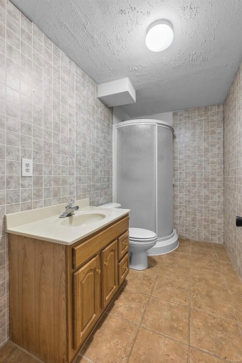 Bathroom featuring vanity, a textured ceiling, tile walls, and a shower stall