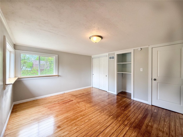 Unfurnished bedroom with baseboards, hardwood / wood-style flooring, a textured ceiling, and visible vents
